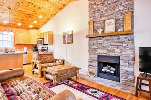 A cozy living room with a stone fireplace, wooden furniture, and a kitchen area with wooden cabinets and a microwave. - Trimont Mountain Cottage (Franklin)