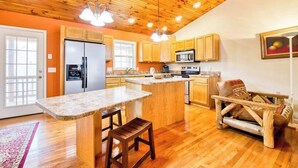 A kitchen with wooden cabinets, a large island with stools, a refrigerator, and a microwave.