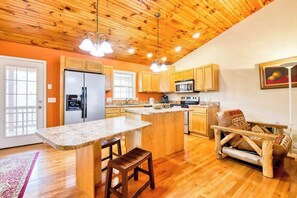 A kitchen with wooden cabinets, a large island with stools, a refrigerator, and a microwave. - Trimont Mountain Cottage (Franklin)
