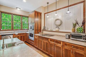A kitchen with wooden cabinets, a sink, a stove, and a window with a view of greenery.