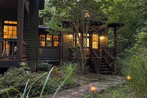 A wooden cabin with a stone pathway, wooden deck, and a staircase leading to a covered porch.
