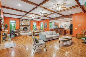 A spacious living area with a fireplace, wooden beams, and a kitchen in the background.