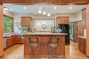A kitchen with wooden cabinets, a central island with bar stools, pendant lighting, and a refrigerator.