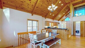 Ein geräumiger Essbereich mit Holztisch und -stühlen, im Hintergrund eine Küche und eine hohe Decke mit Holzbalken.