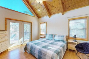 A bedroom with a large bed, wooden ceiling beams, a dresser, a chair, and a window with blinds. - Mountain Hideaway (Almond)