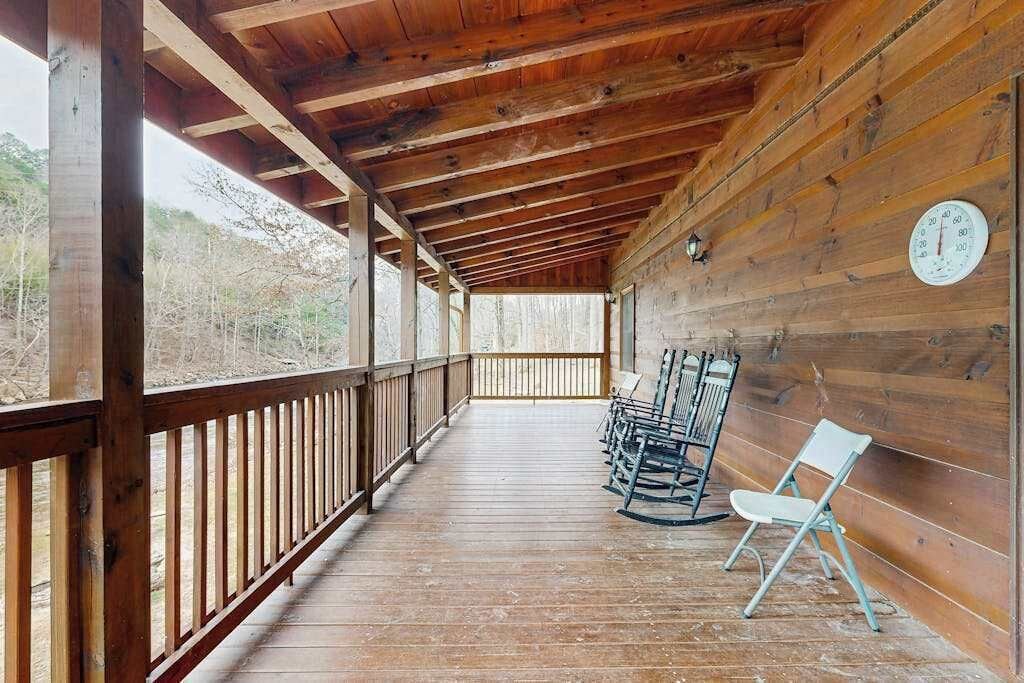 A wooden deck with a railing, a clock on the wall, and a row of rocking chairs.