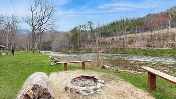 Un terrain de camping équipé d’un foyer, de bancs et situé près d’une rivière.