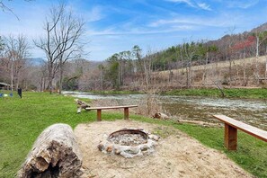 A campsite with a fire pit, benches, and a river. - The Orr House (Sylva)