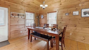 Ein Holzinterieur mit Esstisch, Stühlen, einer Bank, einer Chandelierleuchtre und gerahmten Bildern an den Wänden.