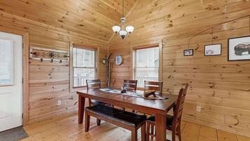 Un intérieur en bois comprenant une table à manger, des chaises, un banc, un lustre et des tableaux encadrés accrochés aux murs.