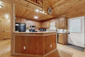 A wooden interior with a kitchen island, wooden cabinets, and a door. - The Orr House (Sylva)