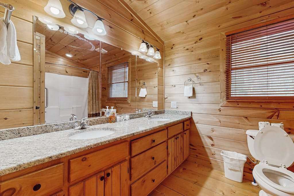 A wooden cabin bathroom with a double sink vanity, a toilet, and a large mirror.
