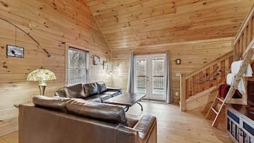 L’intérieur d’un chalet en bois, avec un canapé en cuir, une table et un escalier.