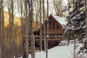 Eine Blockhütte mit mehreren Ebenen, umgeben von schneebedeckten Bäumen.
