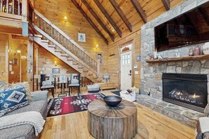 Ein Holzblockhaus-Interieur mit Kamin aus Stein, einer Holztreppe und einer gemütlichen Sitzecke.