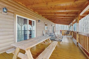 Eine Holzterrasse mit Picknicktisch und -stühlen, einer Glastür und einem Geländer.