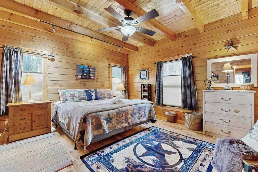 A wooden cabin bedroom with a bed, dresser, and ceiling fan.