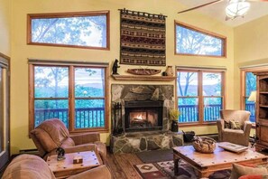 Ein gemütliches Wohnzimmer mit Kamin, großen Fenstern und Blick ins Freie.