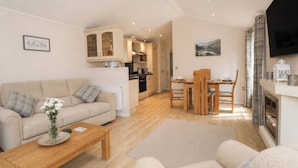A modern living room with a sofa, coffee table, and a dining area with chairs and a table. - Tiggywinkle Beck - White Cross Bay (Windermere)