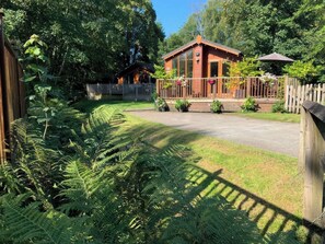 Eine Holzhütte mit Veranda, umgeben von üppiger Vegetation und einem Holzzaun.