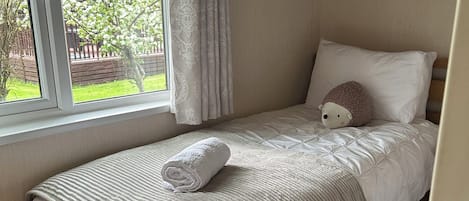A single bed with a rolled white towel, a white pillow, and a stuffed animal.