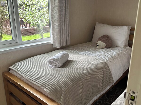 Ein Einzelbett mit einem gerollten weißen Handtuch, einem weißen Kissen und einem Stofftier.