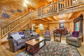 Ein Holzblockbau-Innenraum mit Treppe, einem Wohnzimmer mit Sofa und Sesseln, einem Essbereich und einer Küche.
