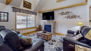 Una sala de estar con chimenea, sofás de cuero, ventilador de techo y vigas de madera.