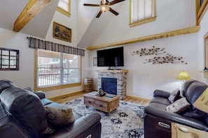 A living room with a fireplace, leather sofas, a ceiling fan, and wooden beams. - The Mountain Haven (Maggie Valley)