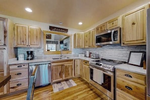 A kitchen with wooden cabinets, a stainless steel refrigerator, a microwave, a stove, and a dishwasher. - The Mountain Haven (Maggie Valley)