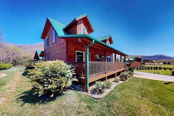 A wooden cabin with a porch, surrounded by a well-maintained lawn and a clear sky. - The Mountain Haven (Maggie Valley)