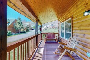 A wooden cabin with a porch, a rocking chair, and a view of a road and houses. - The Mountain Haven (Maggie Valley)