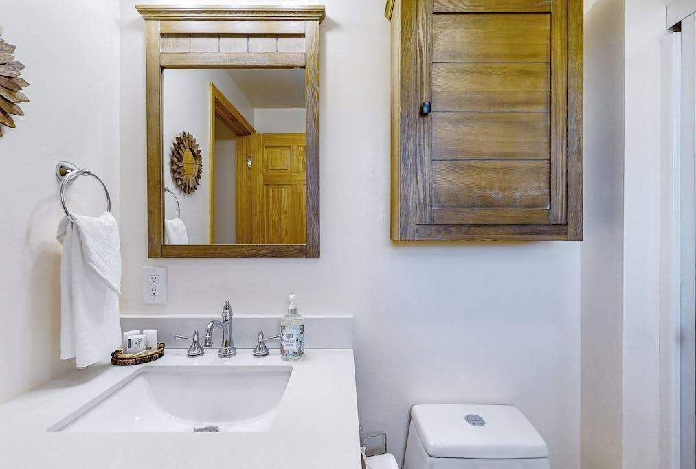 A bathroom with a white sink, a mirror, a wooden door, and a toilet.