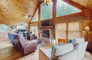 Ein Holzblockhaus-Interieur mit Kamin aus Stein, Ledersofas und großen Fenstern.