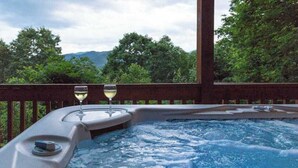 Een hottub met twee glazen witte wijn, omringd door een houten terras en weelderige begroeiing.