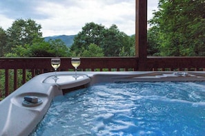 Ein Whirlpool mit zwei Weingläsern, umgeben von einer Holzterrasse und üppiger Vegetation.
