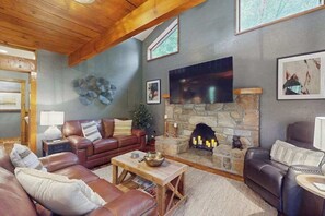 Ein gemütliches Wohnzimmer mit Kamin aus Stein, Ledersofas und einem Flachbildfernseher.