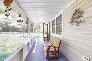 Eine überdachte Veranda mit einer hölzernen Bank, einem dekorativen Wandelement und Blick ins Freie.