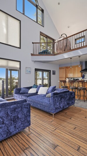 Uma sala de estar moderna com um amplo sofá azul, piso de madeira e vista para o exterior.