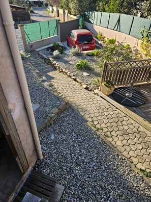 Ein Wohnweg mit rotem Auto, einem verschlossenen Eingangstor und einem gepflasterten Weg zu einem Holztor.