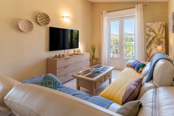 A modern living room with a sofa, a coffee table, a TV, and a balcony with a view.