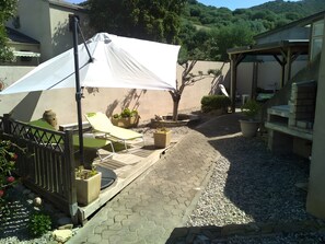 Eine Terrasse mit überdachter Sitzgelegenheit, einem Pergola und einem gepflasterten Weg.