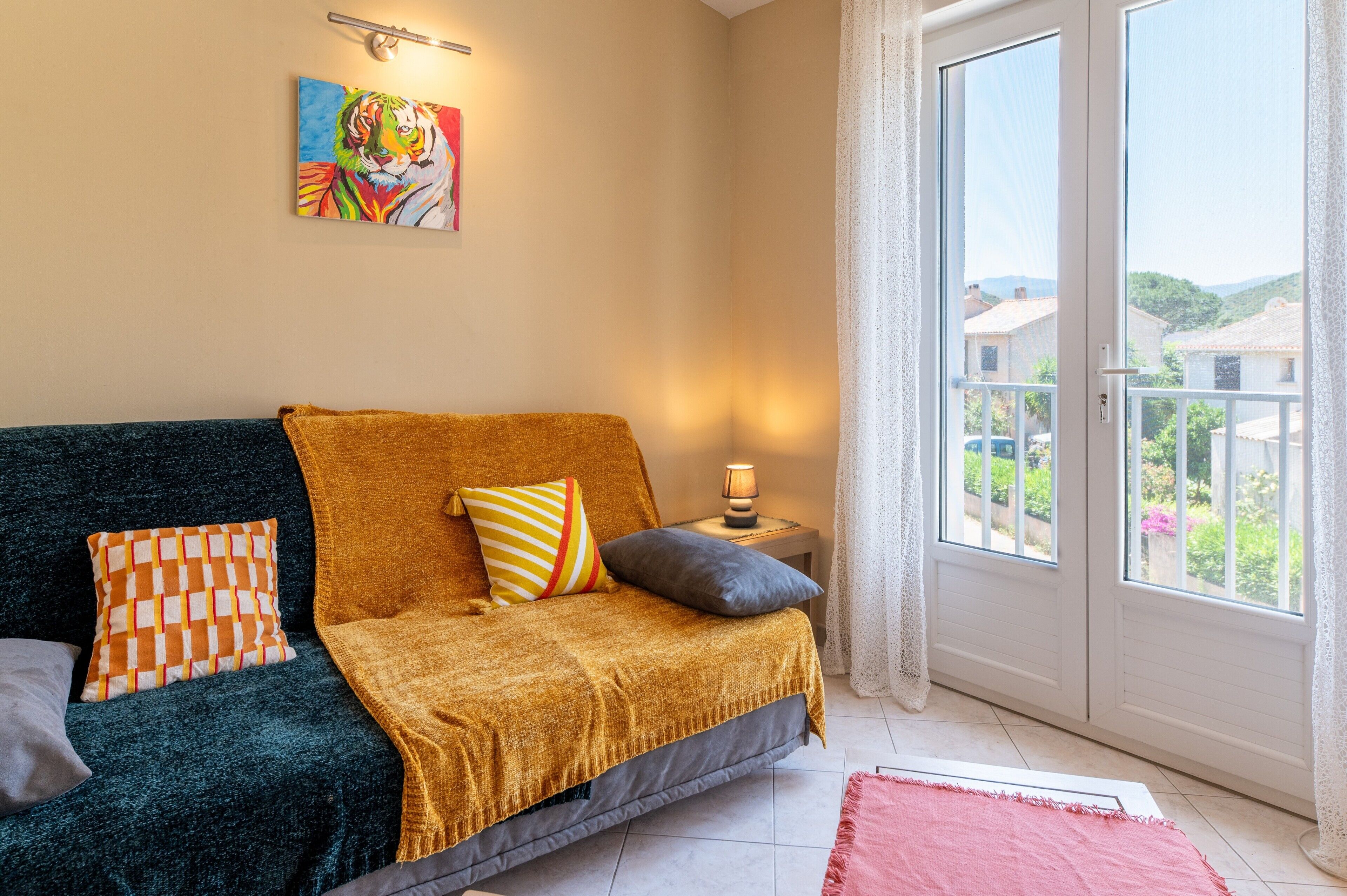 A room with a dark green sofa, a mustard-colored throw blanket, and a painting of a tiger on the wall.