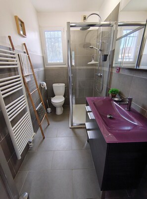 A modern bathroom with a glass shower enclosure, a white toilet, a purple vanity, and a radiator.
