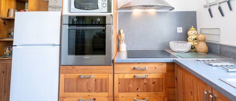 A kitchen with wooden cabinets, a white refrigerator, a built-in oven, a microwave, and a stainless steel range hood.