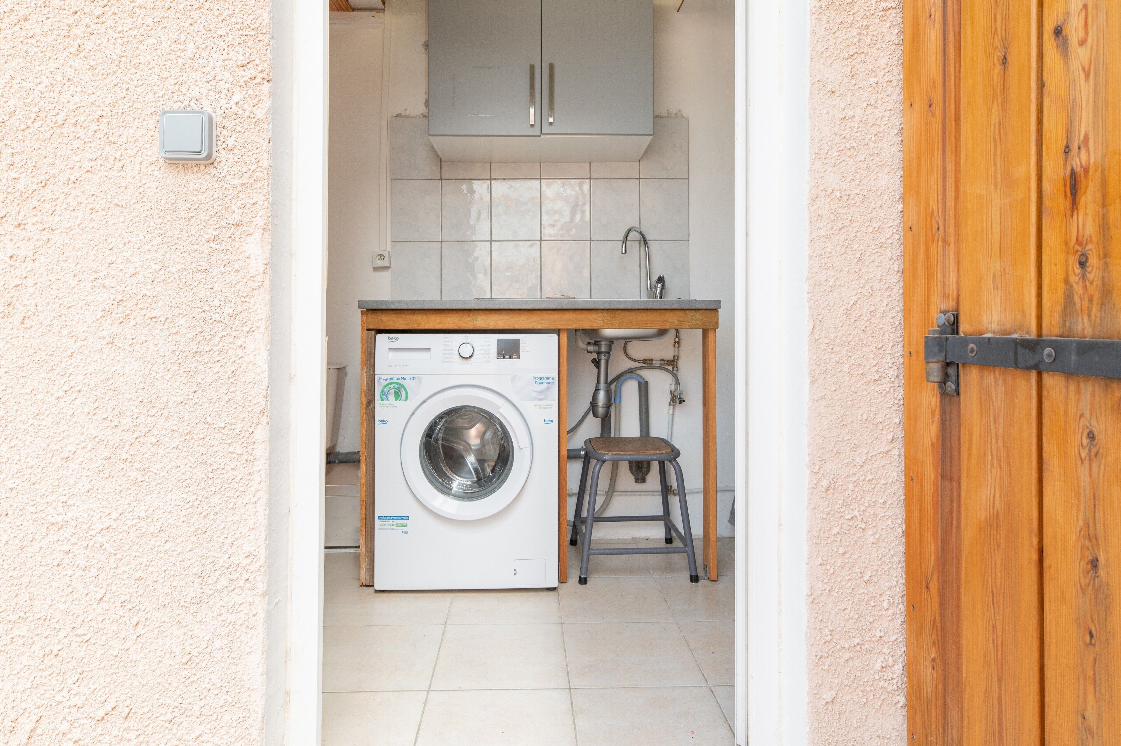 Een wasruimte met een wasmachine, een wasbak en een houten kruk.