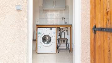 Een wasruimte met een wasmachine, een wasbak en een houten kruk.