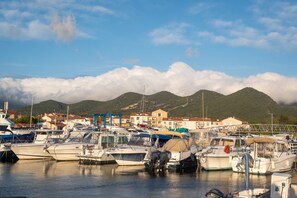 Un port de plaisance avec des bateaux amarrés, un paysage montagneux en arrière-plan et des bâtiments visibles au loin.