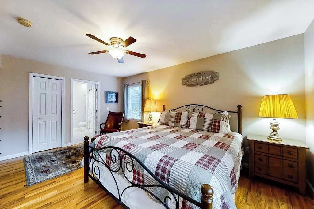 A bedroom with a bed, a ceiling fan, a nightstand, a lamp, a chair, and a door.