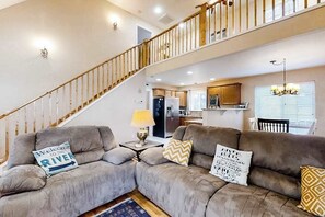 A living room with a sofa set, a lamp, a rug, a staircase, and a kitchen in the background. - Full Steam Ahead (Whittier)